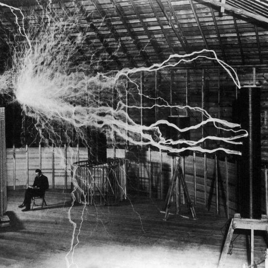 Nikolas Tesla reading a book amongst one of his experiments